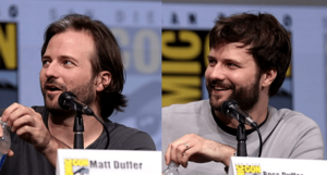 Matt Duffer on the left, with Ross Duffer on the right, both seated behind a table with name cards in front of them and looking to the viewer's left, with a San Diego Comic-Con BBanner in the background