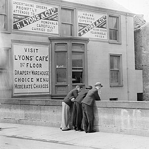 Three men at bridge - ads on wall for Lyons cafe and goods. (24638969284)