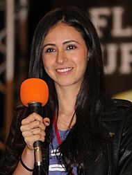 A woman holding a microphone and smiling towards the camera.