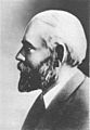A black-and-white profile photograph of the head and shoulders of a middle-aged bearded man, facing left