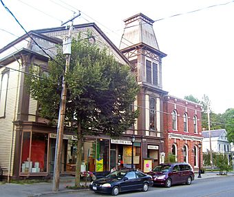 A large building with brown peaked roofs and stucco and half-timber face. There is a brick building next to it on a street corner.