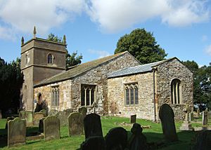 A stone church seen from the southeast, with a small chancel, a larger nave and south aisle under one roof beyond, and a short, rendered tower with pinnacles