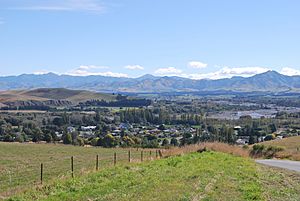 A small town set in a valley seen from one of the surrounding hills. A shingle river is in the background