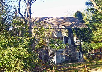 A stone house with some ivy on the front and a triangular-roofed rear wooden porch partially obscured by shrubbery on the left