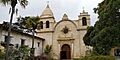 Photograph of the bell tower of Carmel Mission, with a peaked dome atop with gardens in the foreground.