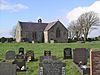 At the far end of a graveyard is a simple stone church, which appears L-shaped, and has a bellcote