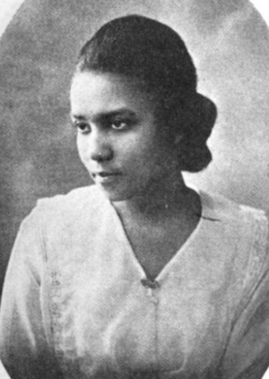A young African-American woman wearing her hair in a chignon, and wearing a white loose-fitting blouse or dress with a v-neck