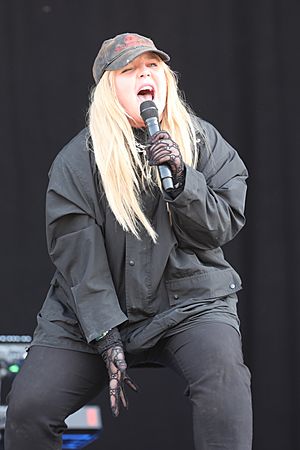Artist is singing into hand-held microphone, wearing dark grey jacket and pants.
