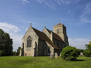 A flint/rubble church seen from the south with a red tiled roof, embattled tower with 'Hertfordshire spike' spire and a south aisle with a porch