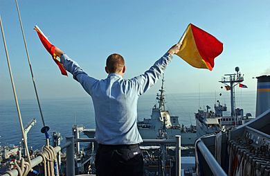 US Navy 051129-N-0685C-007 Quartermaster Seaman Ryan Ruona signals with semaphore flags during a replenishment at sea
