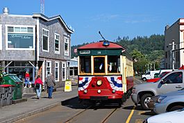 Red streetcar with creamy-white windowpanes on trolley tracks in narrow Astoria street, with green, forested hills in the background