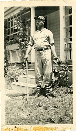 A man in a baseball uniform holding a baseball bat and glove outside a house