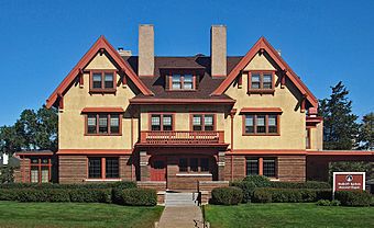 Wide two-and-a-half-story house with symmetrical gables flanking a central bay with a porch and balcony