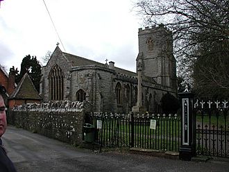 Stone building with arched window and square tower, separated from the road by a stone wall and railings.