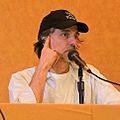 Upper body shot of man sitting behind desk with baseball cap speaking into a microphone