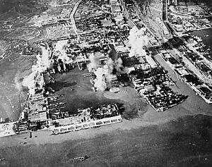Black and white aerial photograph of a harbour with smoke rising from several locations