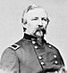 Head and shoulders of a white man with a Van Dyke mustache and beard, wearing a double-breasted military jacket with a rectangular patch over the shoulder.