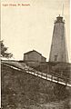 Black and white postcard of the wooden lighthouse at the top of the harbour at Port Burwell, ON. The road runs down to the bridge over Otter Creek
