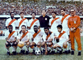 Photo of twelve men, seven standing and five crouching, inside a stadium