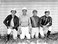 Four jockeys kneeling in the grass in front of a stable, Washington State (4951163393)