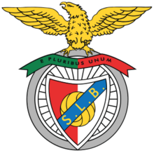 Looking to its right, a wingspread golden eagle stands atop a bicycle wheel's grey tire. Below, on the spoked wheel, a horizontal green and red strip reads "E PLURIBUS UNUM", and a diagonal blue strip with the golden initials "S. L. B." overlays a red and white shield with a golden football on its centre.