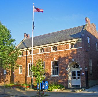 A 1+1⁄2-story brick building with a flagpole in front, lit from the right by late afternoon sun