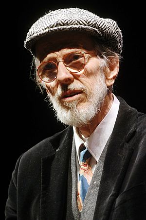 An elderly man with a white beard, round glasses, and beret-like hat.
