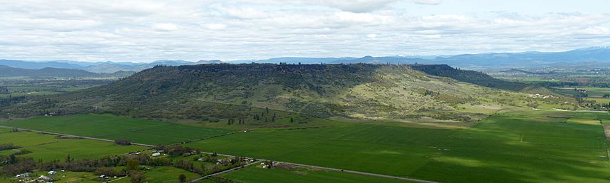 A large flat topped plateau with trees scattered on its flanks and farmland below it