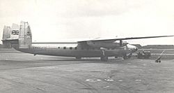 A twin-engine airliner with three fins parked on ramp while being serviced, with mobile staircases nearby.