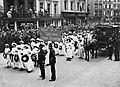A procession of Suffragettes, dressed in white and bearing wreaths and a banner reading "Fight on and God will give the victory" during the funeral procession of Emily Davison in Morpeth, Northumberland, 13 June 1913. Crowds line the street to watch.