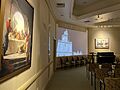 The St. George Visitors Center theatre, playing a movie on the history of the temple. Chairs are shown in the foreground, to the side are two paintings of the life of Jesus Christ.