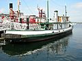 Photograph of the tug Arthur Foss at dock on Lake Union as a museum ship, white with green trim, showing the stern and a view across the lake.