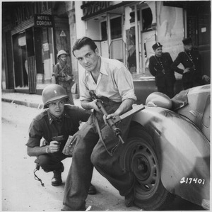 American officer and French partisan crouch behind an auto during a street fight in a French city. - NARA - 531322