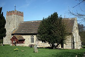 A mainly stone church seen from the south showing a tower with a battlemented brick parapet, a porch, and a roof with red and black tiles in bands