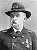Head and shoulders of a white man with a drooping mustache, wearing a cavalry hat and a double-breasted military jacket with two medals pinned to the left breast.