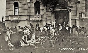 Black and white photograph of a group of men wearing sombreros surrounding a stone building.  Dated 5/15/1911.