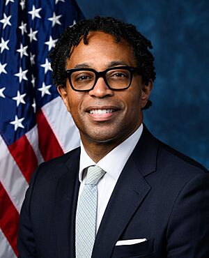 Official House portrait of Bell smiling in front of the U.S. flag, wearing a black suit, white shirt, and light green plaid tie.