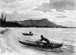 Two natives with outrigger canoes at shoreline, Honolulu, Hawaii