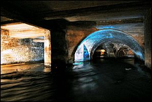 Enclosed arches underneath a building with flowing water passing through