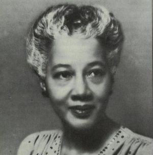 Black and white portrait of a middle-aged African woman with greying hair in a v-necked and pleated blouse or dress.