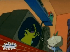 A bald cartoon baby wearing a blue shirt and a diaper stands smiling at a television displaying a large green dinosaur.