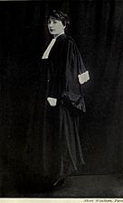 A full-length, black-and-white photograph of a woman wearing judicial robes