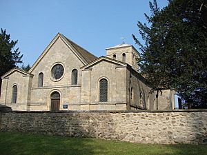 The west end of a stone church with three gable ends, a circular window and a doorway and more windows with round heads