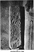 A rectangular stone, stood on one end, with carvings of a man on a horse, another horse, geometric designs and some letters.