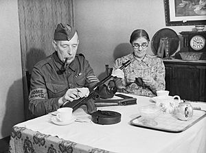 A veteran sergeant in the Dorking Home Guard cleans his Tommy gun at the dining room table, before going on parade, 1 December 1940. H5850