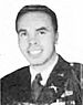 A young man in his army dress uniform with no hat. He appears to be in a seated position and is smiling.