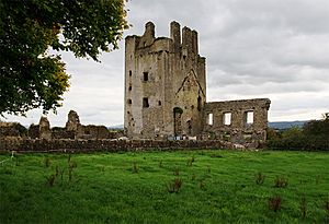 A photo of a ruined, square, thick-walled tower and an adjacent house of which only one wall with big windows remains