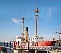 Photograph of Lightship No. 83, Relief, at dock in Seattle as a museum ship, its light masts rising to the sky and its red hull painted with its contemporary name Swiftsure.