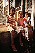 Three children sit on the porch of a run-down home