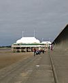 Short pier above sand, surmounted by white pavilion with flag poles.